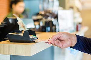 person swiping card through machine with cashier in the background